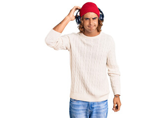 Naklejka premium Young hispanic man listening to music using headphones confuse and wonder about question. uncertain with doubt, thinking with hand on head. pensive concept.