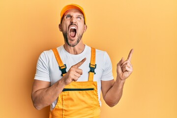 Young handsome man wearing handyman uniform pointing to the side angry and mad screaming frustrated and furious, shouting with anger looking up.