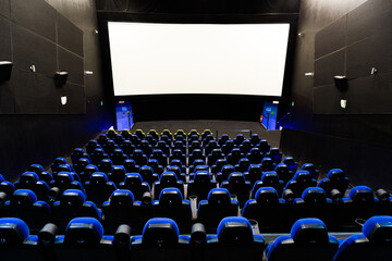 Cinema theater interior with screen and blue seats. Wide shot view from the back of an empty auditorium with lights on stock photo.