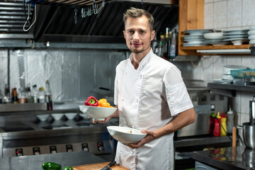 Happy young professional chef in white uniform holding bowls with fresh capsicum