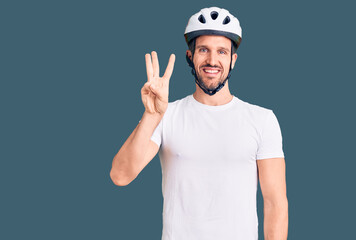 Young handsome man wearing bike helmet showing and pointing up with fingers number three while smiling confident and happy.