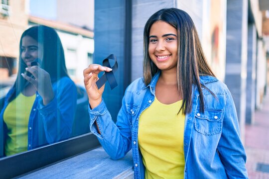 Young latin woman smiling happy holding black ribbon at city.