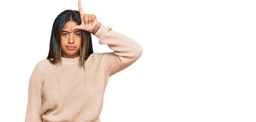 Young latin girl wearing wool winter sweater making fun of people with fingers on forehead doing...