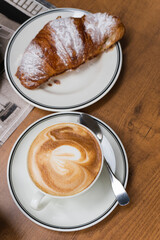 Cup of cappuccino coffee and croissant close-up top view. Appetizing delicious breakfast