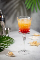 Colourful exotic Tequila Sunrise cocktail in a glass served with ice on gray background