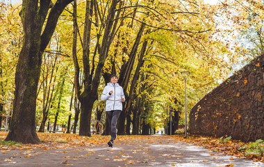 Fit athletic woman have a jogging in the autumnal city park. Young fitness female smiling and...