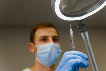 Doctor holds a syringe with a drop of medication at the end of the needle. Preparation before...