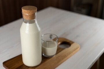 milk bottle and a glass on the kitchen table. Milk on a wooden board indoors.Organic farmer's Breakfast