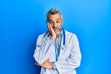 Middle age grey-haired man wearing doctor uniform and stethoscope thinking looking tired and bored...
