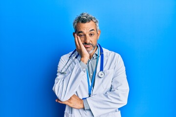 Middle age grey-haired man wearing doctor uniform and stethoscope thinking looking tired and bored with depression problems with crossed arms.