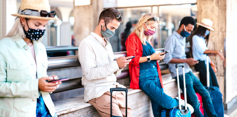 Multiracial friends wearing face mask using mobile smart phones - Young millenial checking online reservations at train station - New normal travel and lifestyle concept - Vivid contrast filter
