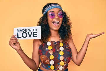 Young african american woman wearing bohemian and hippie style holding made with love message celebrating victory with happy smile and winner expression with raised hands