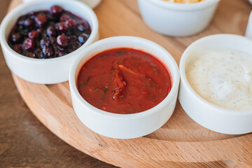 A set of sauces in white bowls on a wooden stand. Creamy, ginger, tomato and grated cheese. Hot pepper sauce