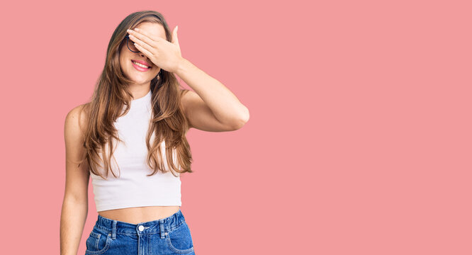 Beautiful caucasian young woman wearing casual clothes and glasses smiling and laughing with hand on face covering eyes for surprise. blind concept.