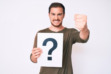 Young handsome man holding question mark annoyed and frustrated shouting with anger, yelling crazy with anger and hand raised