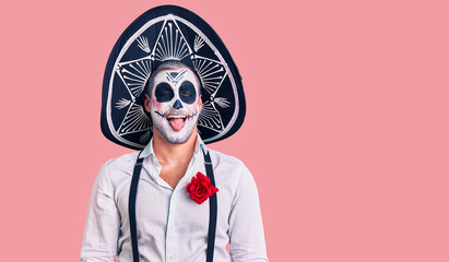Man wearing day of the dead costume over background sticking tongue out happy with funny expression. emotion concept.
