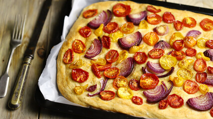 Fresh homemade focaccia on a pan with tomatoes and blue onions. Italian cuisine at home. Focaccia recipe.