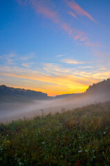 Beautiful summer hazy landscape with foggy hollow and green hills before the sunrise.