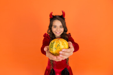 pumpkin vegetable in hands of happy devil kid wear horns costume of imp on halloween party,...