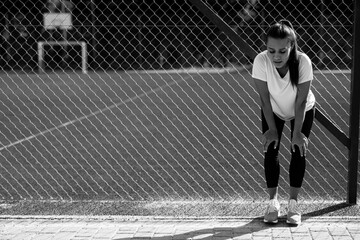 Exhausted woman in sport clothing resting at stadium