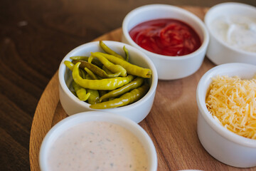 A set of sauces in white bowls on a wooden stand. Creamy, ginger, tomato and grated cheese. Hot pepper sauce