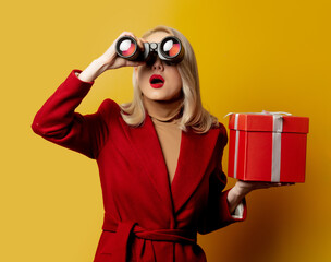 woman in red coat with binoculars and gift box on yellow background