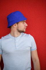 Young handsome man with a beard in a panama hat on his head against the background of a red wall. Portrait of a guy in a white t-shirt