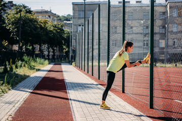 Flexible woman stretching legs near chain link fence