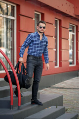 Young male businessman with a beard walks with a bag on the steps. Handsome guy in shirt and glasses