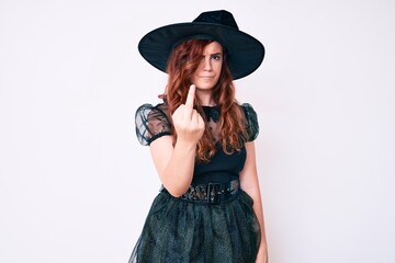 Young beautiful woman wearing witch halloween costume showing middle finger, impolite and rude fuck off expression