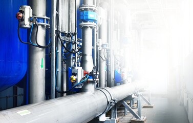 Large industrial water treatment and boiler room. Shiny steel metal pipes and blue pumps and valves.