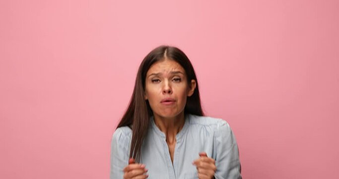 hyperactive casual woman in blue denim shirt making funny faces, acting shocked, screaming and making hands gestures on pink background