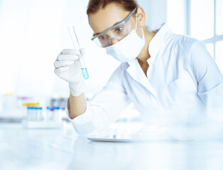 Female laboratory assistant analyzing test tube with blue liquid. Medicine, health care and researching concept