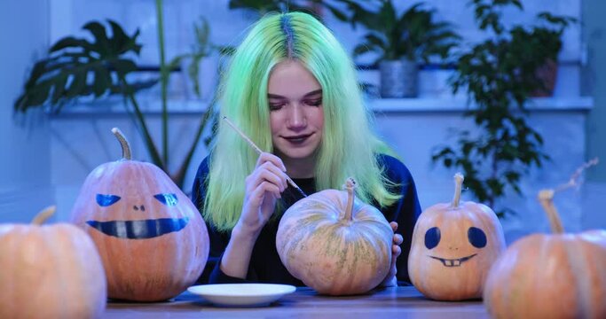  Preparation of Halloween party, young teenager girl with scary witch make-up drawing on pumpkins 