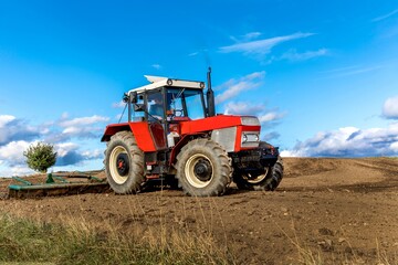 Agriculture red tractor cultivating field over blue sky. Old red tractor in the agricultural field; mechanism. Tractor plowing land. Harvester sowing wheat.