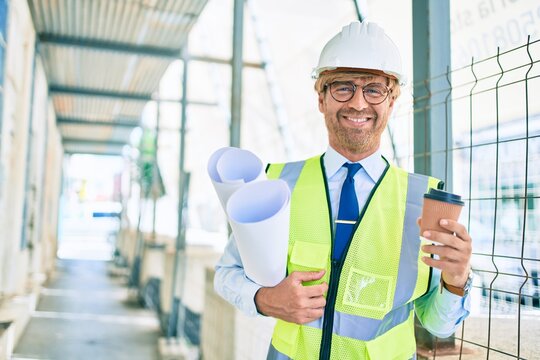 Business architect man wearing hardhat standing outdoors of a building project wearing reflective vest drinking a cup of coffee