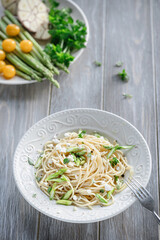 Spaghetti with fresh vegetables, yellow tomatoes, asparagus, parsley and garlic in a plate on a light background. Italian pasta Primavera style.