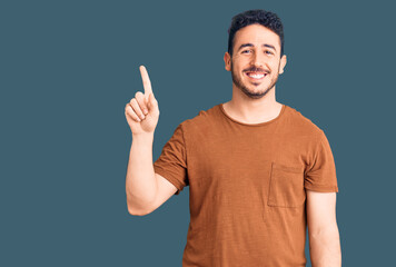Young hispanic man wearing casual clothes showing and pointing up with finger number one while smiling confident and happy.