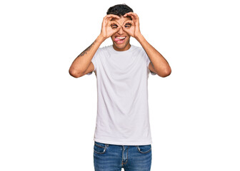 Young handsome african american man wearing casual white tshirt doing ok gesture like binoculars sticking tongue out, eyes looking through fingers. crazy expression.