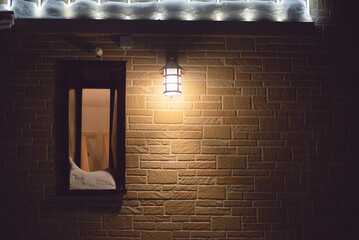 House window in a snow and burning lamp on the brick wall background with copy space.