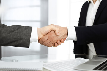 Unknown diverse business people are shaking hands finishing up meeting at the desk in office, close-up. Handshake concept