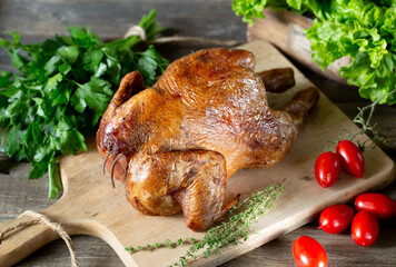 Smoked chicken on wooden board with tomatoes and greens