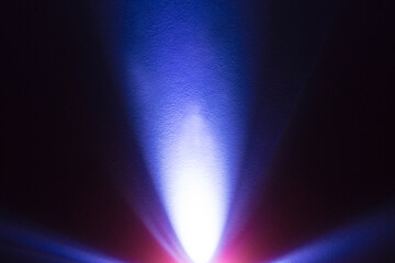 Cool blue light from an LED flashlight on a white wall. A ray of light on the surface.