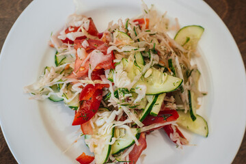 Vegetarian salad of cabbage, cucumbers and tomatoes on a white plate. The dish stands on a dark wooden background. Healthy eating. Diet