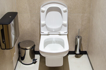 White toilet with the lid raised in the booth of a public toilet. Public restroom for men and women.