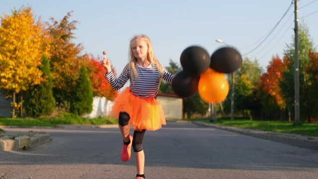 Halloween kids. smiling girl with orange and black balloons. Funny child in carnival costumes celebrating Halloween outdoors. Slow motion.