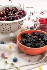 Cherries, raspberries and blackberries in bowls on a pink background