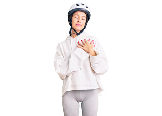 Beautiful brunette young woman wearing bike helmet and sporty clothes smiling with hands on chest with closed eyes and grateful gesture on face. health concept.