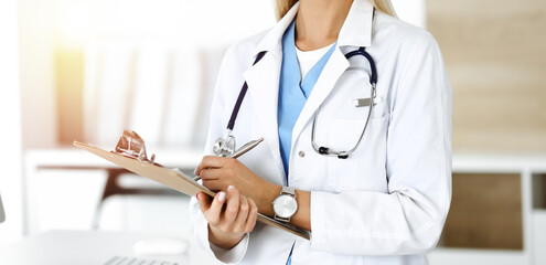 Unknown woman-doctor at work in sunny clinic. Female physician controls medication history record, close-up. Medicine concept