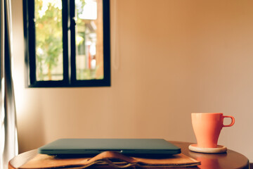 Orange coffee cup and laptop on the table in the cafe.